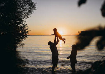 Mother with father holding son in front of sea at sunset